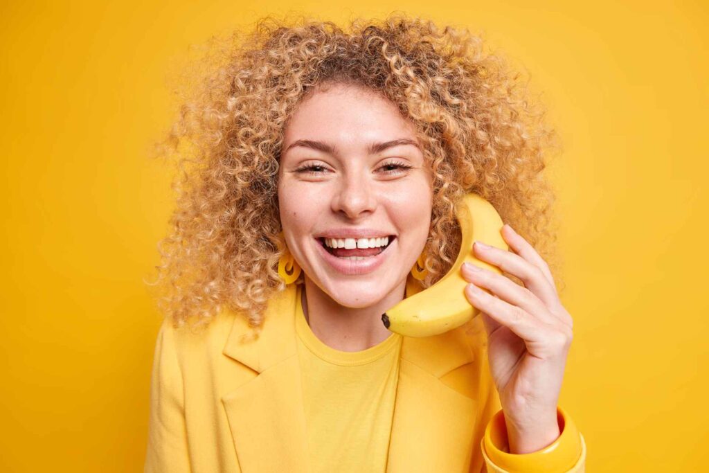 05 Una chica sonriendo con una banana en la mano sobre fondo amarillo intenso