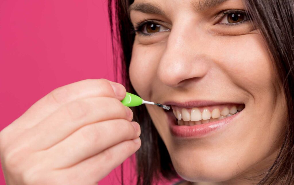 06 Una mujer sonriente limpiandose los dientes con un cepillo interdental o interproximal